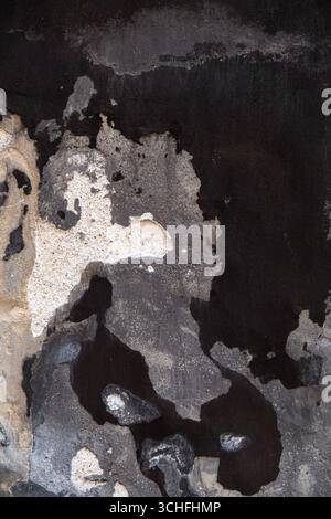 Alte schwarze, graue und weiße, rissige Lackstruktur, die sich von der Betonwand löst. Hintergrundbild. Stockfoto