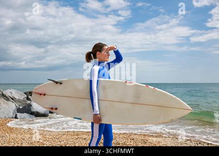 Frau mit Surfbrett an einem sonnigen Strand, mit Blick auf das Meer Stockfoto