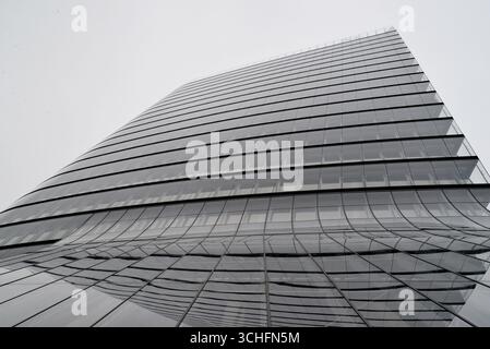 Moderner Wolkenkratzer aus Glas mit geschwungenen Linien an bewölktem Tag. Stockfoto
