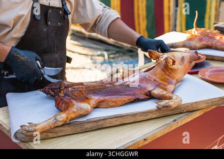 Der Koch in mittelalterlichen Gewändern bereitet ein gebratenes Ferkel zu, das während des Festivals serviert wird. Stockfoto