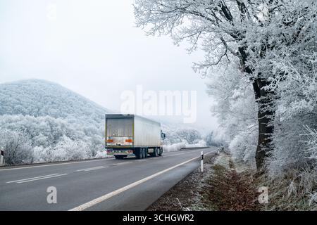 Ein Lkw fährt auf der schneebedeckten Straße durch eine magische weiße Winterlandschaft und liefert Lebensmittel und Vorräte für die Weihnachtszeit Stockfoto