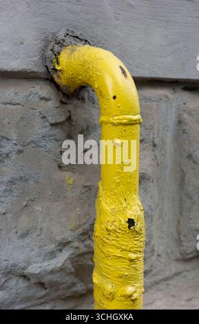 Nahaufnahme einer gelben Gasleitung an einer strukturierten grauen Wand mit Anzeichen von Verschleiß. Stockfoto
