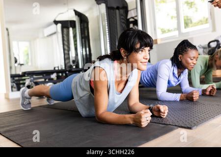Verschiedene Freundinnen, die im Fitnessstudio trainieren, Plank auf Yogamatten machen, konzentriert und entschlossen, zu Hause Stockfoto