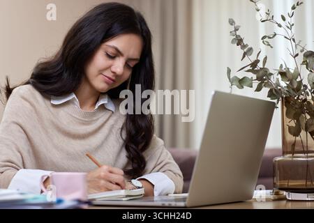Glückliche positive Frau, die im Wohnzimmer von zu Hause aus mit einem Laptop arbeitet Stockfoto