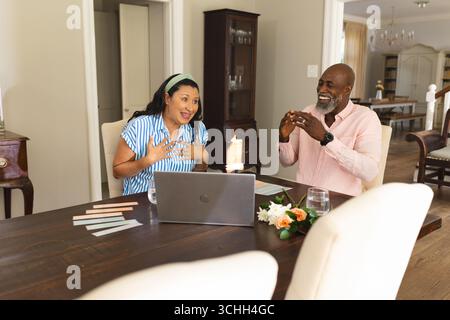Seniorenpaar feiert zu Hause und plaudert fröhlich über Laptop mit Kerzen Stockfoto