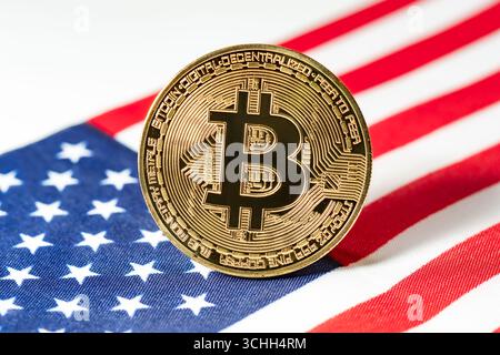 Eine Makroaufnahme einer physischen goldenen Bitcoin-Münze auf einem verschwommenen Hintergrund der amerikanischen Flagge. Stockfoto