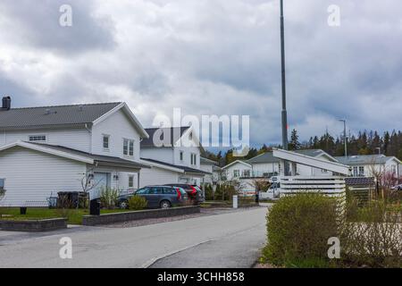 Moderne weiße Häuser mit Autos auf Vorstadtstraße vor dem Hintergrund des bewölkten dramatischen Himmels. Schweden. Stockfoto