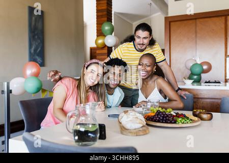 Lächelnde, vielfältige Freunde, die zu Hause Snacks und Getränke genießen und gemeinsam feiern Stockfoto