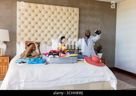 Koffer auf dem Bett packen, afroamerikanische Familie bereitet sich auf den Urlaub vor, fühlt sich aufgeregt, wie zu Hause Stockfoto