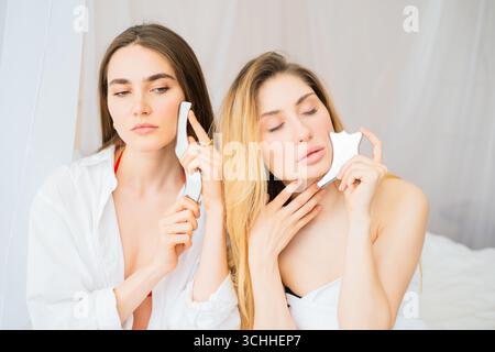 Junge niedliche Frauen üben Gesichtsmassage mit Gua Sha Tools für Hautpflege Routine Stockfoto