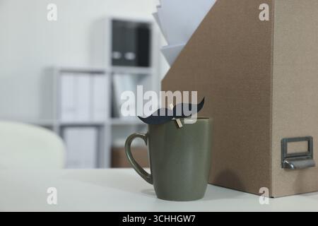 Alles Gute zum Vatertag. Tasse mit Papierschnurrbart auf weißem Tisch drinnen Stockfoto