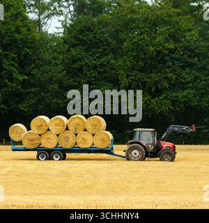 Traktor und Frontlader auf dem Feld geparkt (Seitenansicht). Ungewickelte kreisförmige Strohballen, die bei der Ernte geladen gesammelt wurden – Farnley, North Yorkshire, England, Vereinigtes Königreich. Stockfoto