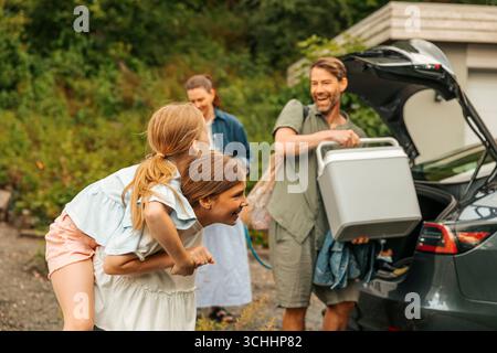 Glücklicher Mann, der Kühler in den Kofferraum lädt, während er die Tochter ansieht Stockfoto