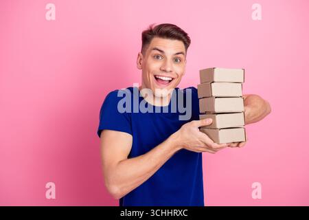 Glücklicher junger Mann in blauem T-Shirt, der kleine Pappschachteln vor hellrosa Hintergrund hält Stockfoto