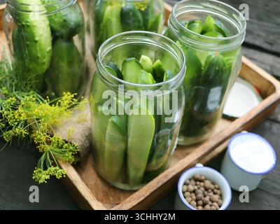 Köstliche eingelegte Gurken in einem Glas in einer Holzkiste, Gewürze, Kräuter auf einem Tisch. Herstellung von Gurken für Gurken für Gurken Stockfoto