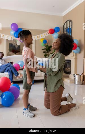 Mutter kniete, lächelte den Sohn im Wohnzimmer an, dekoriert mit bunten Ballons Stockfoto