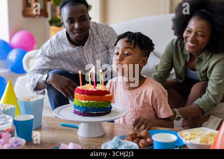 Kerzen auf buntem Kuchen ausblasen, Afroamerikaner mit lächelnden Eltern Stockfoto