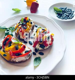 Sandwiches oder Toasts mit gegrillter Paprika, Frischkäse, Sonnenblumenkernen, Olivenöl und Basilikumblättern auf weißem Hintergrund. Gesundes und vegetarisches Gericht. Stockfoto