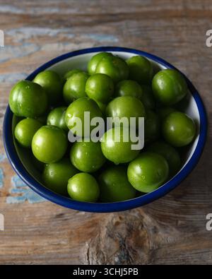 Nahaufnahme frischer grüner Pflaumen in einer weißen Emailschüssel mit blauem Rand Stockfoto