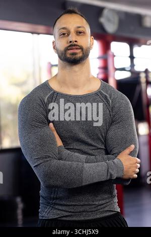 Indischer Mann, der mit gekreuzten Armen im Fitnessbereich steht, mit Boxringseilen, Gewichten Stockfoto