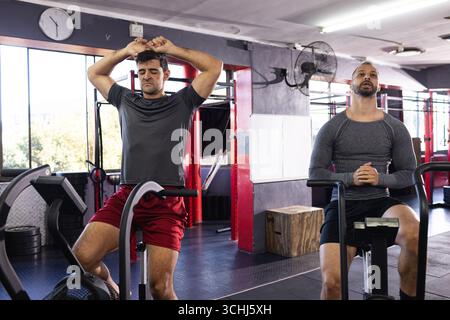 Verschiedene männliche Trainingsfreunde, die zwischen den Intervallen auf Fahrrädern im Fitnessstudio ruhen Stockfoto
