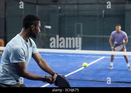 Verschiedene männliche Freunde spielen Pickleball auf dem blauen Platz mit Paddeln, Limettengrüner Kugel, Kopierraum Stockfoto