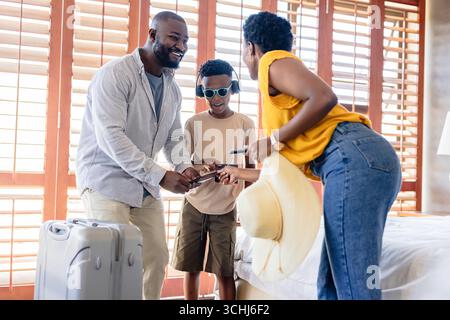 Packen Sie Koffer für den Urlaub, afroamerikanische Familie lächelt zu Hause zusammen Stockfoto