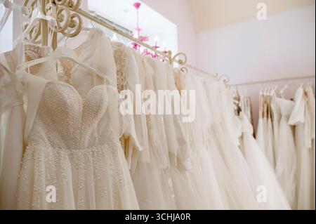 Wunderschöne Brautkleider, Brautkleider hängen an Kleiderbügeln. Modischer Look. Innenraum des Hochzeitssalons. Viele Hochzeitskleider hängen an Kleiderbügeln. Hohe Qualität Stockfoto