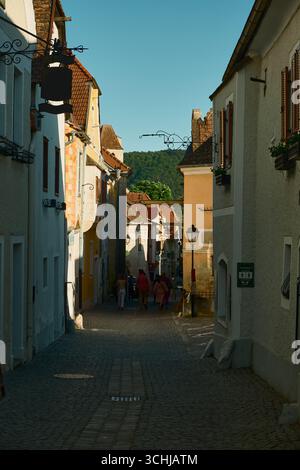 Charmante historische Straße in Dürnstein, Österreich, mit Kopfsteinpflaster und schönen alten Häusern unter einem hellblauen Himmel. Sonnendurchflutete Szene Stockfoto