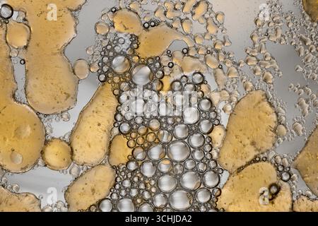 Das Netzwerk aus klaren und gelben Ölblasen bildet gruppierte Kreise über flüssige Makrofotos, die Formen, Texturen und Lichtreflexionen hervorheben. Stockfoto