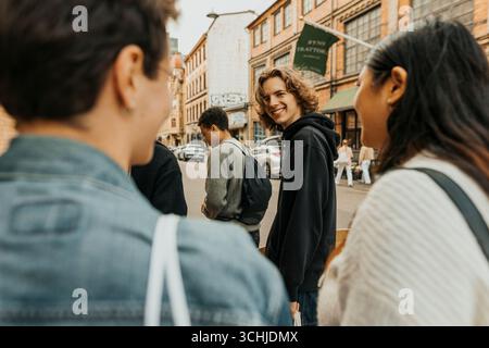 Porträt eines lächelnden jungen Mannes, der über die Schulter schaut, während er mit Freunden auf der Straße spaziert Stockfoto