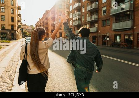 Rückansicht einer sorglosen jungen Frau, die mit einem männlichen Freund an sonnigem Tag auf der Stadtstraße tanzt Stockfoto