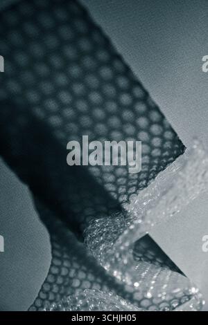 Nahaufnahme der Luftpolsterfolie, die geometrische Schatten auf einer Oberfläche erzeugt. Abstrakte Minimaltextur bei monochromem Licht. Stockfoto