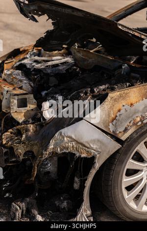 Ein verkohltes Auto parkt auf einem Grundstück und weist schwere Verbrennungsschäden an der Front und der Motorhaube auf. Die Überreste zeigen Zerstörung durch ein Feuer, mit Asche und Stockfoto