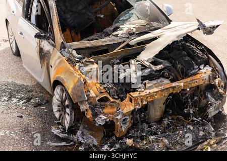 Ein verbranntes Auto sitzt verlassen mit verkohlten Überresten und geschmolzenen Komponenten. Das Wrack weist erhebliche Hitzeschäden auf, wodurch der Motor und der Innenraum sichtbar werden Stockfoto