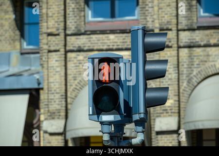 Eine Ampel zeigt eine rote Fußgängerfigur an, die anzeigt, dass das Überqueren der Straße nicht sicher ist. Im Hintergrund befindet sich ein historisches Gebäude mit großer Fläche Stockfoto