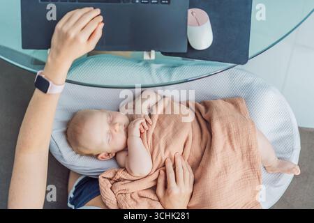 Multitasking-Mutter arbeitet zu Hause an einem Laptop, während ihr neugeborenes Baby friedlich in einem gemütlichen Nest auf ihrem Schoß schläft. Konzept der Fernarbeit, Mutterschaft Stockfoto