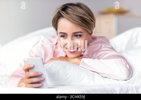Glückliche Frau, die im Bett liegt und Textnachrichten liest Stockfoto