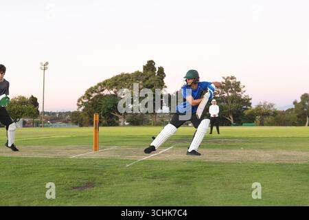 Teenager-Schlagmann in blauem Hemd, der mit Cricketschläger auf dem Rasenplatz einen Schuss spielt, Kopierraum Stockfoto