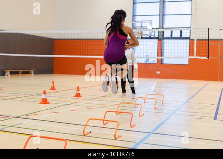 Abwechslungsreiches Trainerinnen- und Athletentraining in der Sporthalle, Hürdenhürden durch Volleyballnetz Stockfoto