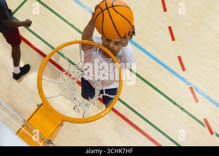 Asiatischer männlicher Basketballspieler, der auf den Basketball springt und den Ball mit Schlangen über dem Platz hält Stockfoto