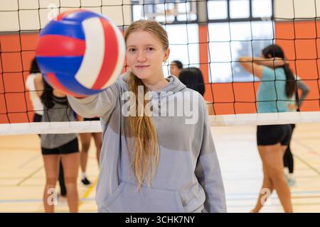 Verschiedene Athleten halten Volleybälle, während sie sich im Fitnessstudio mit Netz dehnen und unterhalten Stockfoto