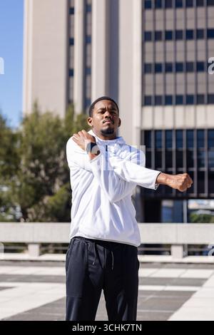 afroamerikaner, der die Arme über die Brust auf dem Dach spannt, in sportlicher Kleidung, Smartwatch Stockfoto