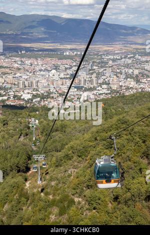 Aus der Vogelperspektive von einer Seilbahn aus zeigt die weitläufige Stadt Skopje in Nordmakedonien, eingebettet in ein Tal mit üppigen grünen Bergen und Wäldern Stockfoto