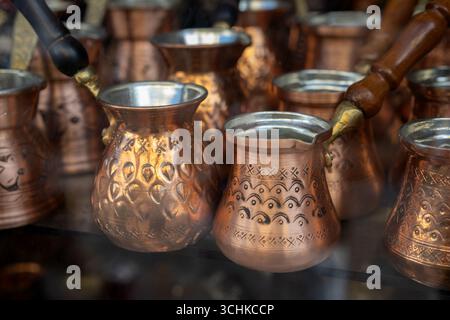 Eine Nahaufnahme mehrerer handgefertigter Kupferkaffeekannen, bekannt als Cezves, mit kunstvollen Mustern und Holzgriffen in einem Markt oder Geschäft Stockfoto