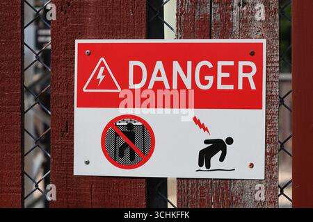 Warnschild für Stromschlaggefahr in Nahaufnahme auf rotem Holzzaun Stockfoto