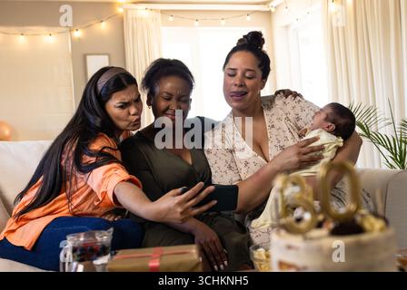 Verschiedene Freundinnen machen Selfie auf der Couch, feiern mit Kuchen und neugeborenes Baby zu Hause Stockfoto