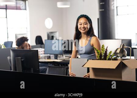 Asiatische Frau lächelt im Büro, packt die Kiste an einem neuen Arbeitsplatz aus Stockfoto