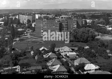 Ein Schwarzweißfoto aus dem Archiv, das im Juli 1997 in Sloviansk aufgenommen wurde. Ein Panoramablick von einem 14-stöckigen Gebäude im Stadtteil Svobody auf die urbane Landschaft, der den starken Kontrast zwischen dem alten privaten Wohnbereich und einem modernen mehrstöckigen Apartmenthaus zeigt. Der Rahmen spiegelt die Merkmale der Stadtplanung und das soziale Gefüge des postsowjetischen Sloviansk in den 1990er Jahren wider Stockfoto