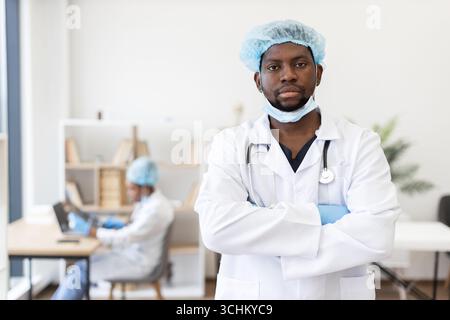 Selbstbewusster männlicher Arzt mit Schutzkleidung im Krankenhaus gekreuzte Arme Stockfoto